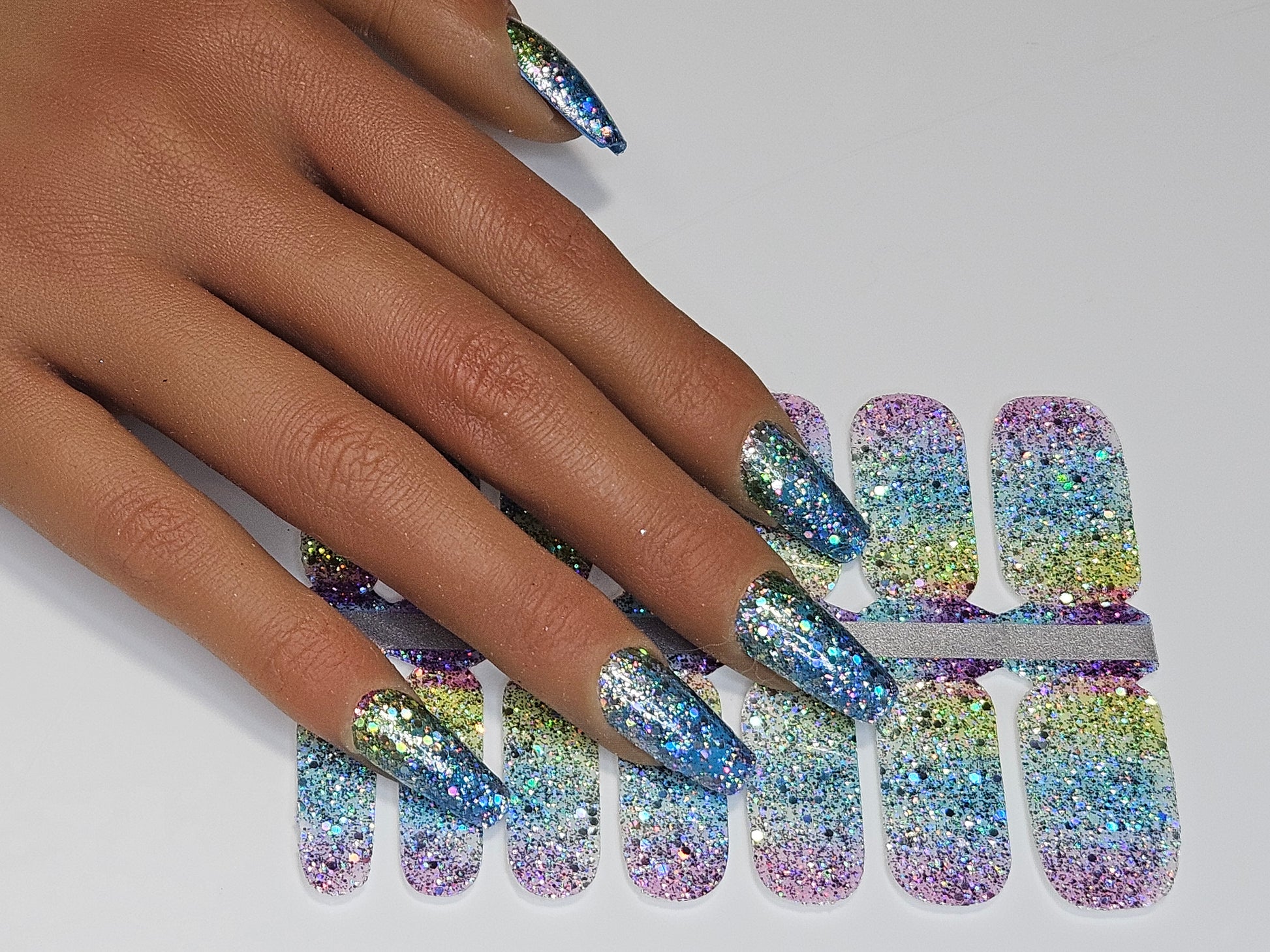 Multicolored glittery nail wraps on a hand with a white background