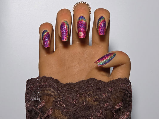 Hand with multicolored glittery handmade press on nails against a plain background