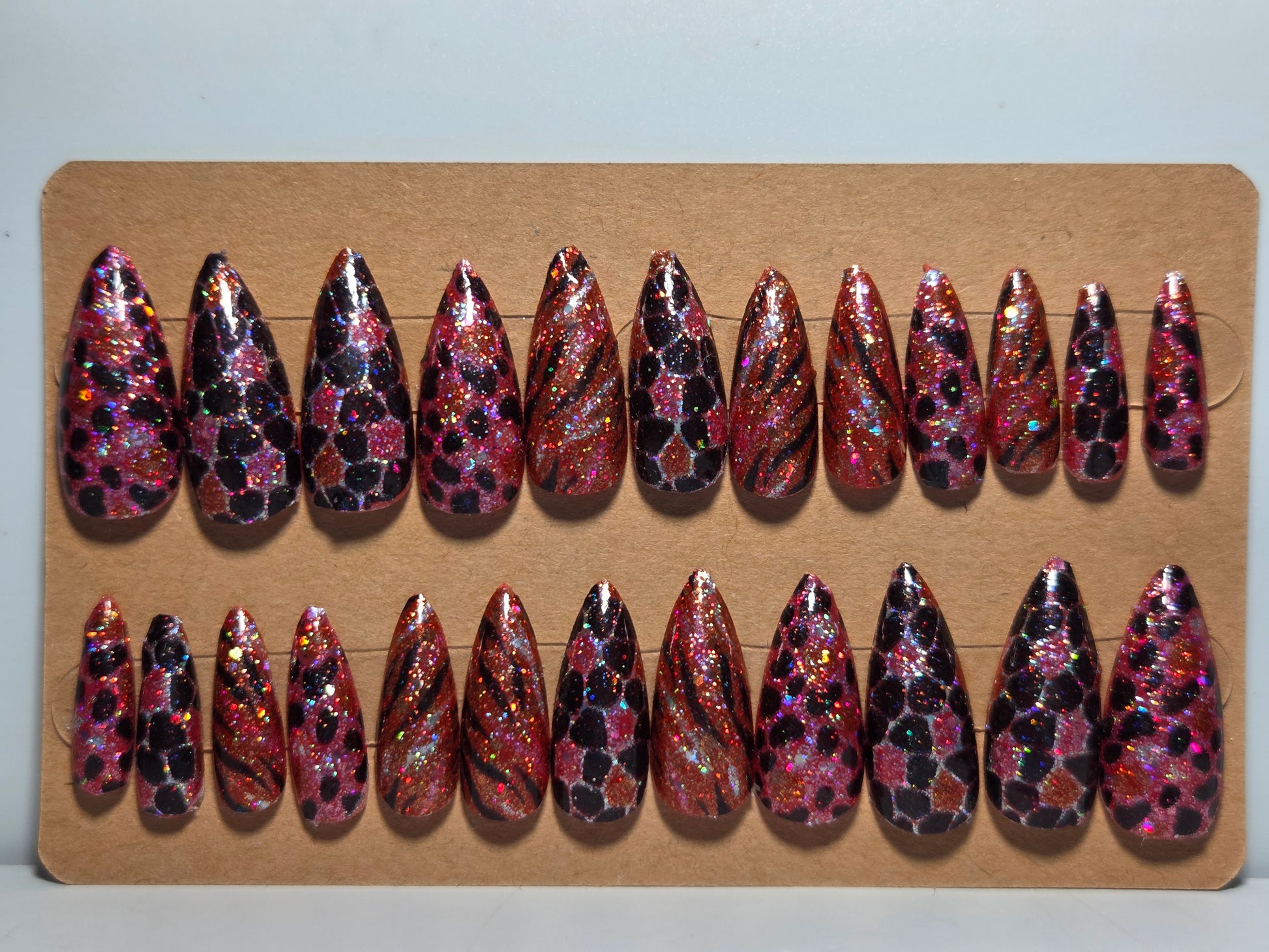 Set of pink and black glitter handmade press on nails on a cardboard display against a plain background