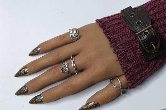 Hand wearing a burgundy knit sleeve with a buckle, multiple rings, and decorative nails on a white background