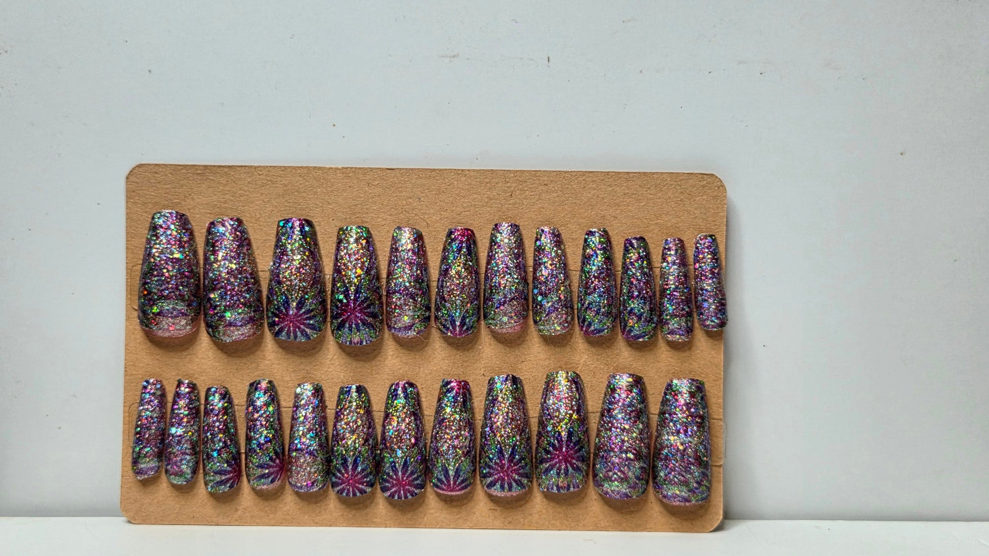 Set of press-on nails with multicolor designs on a wooden board against a white background
