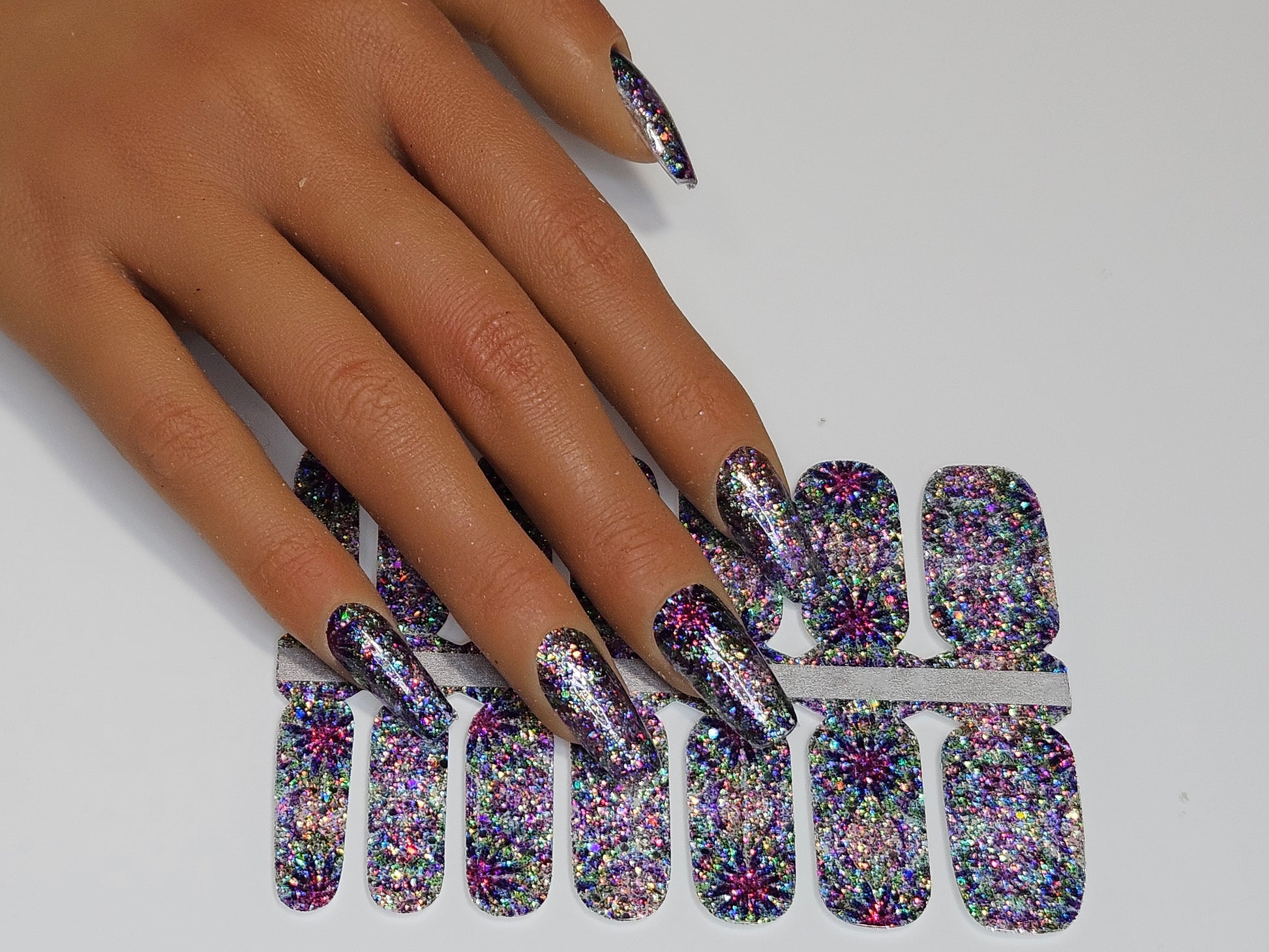 Multicolored glittery nail art sheets on a hand with a white background