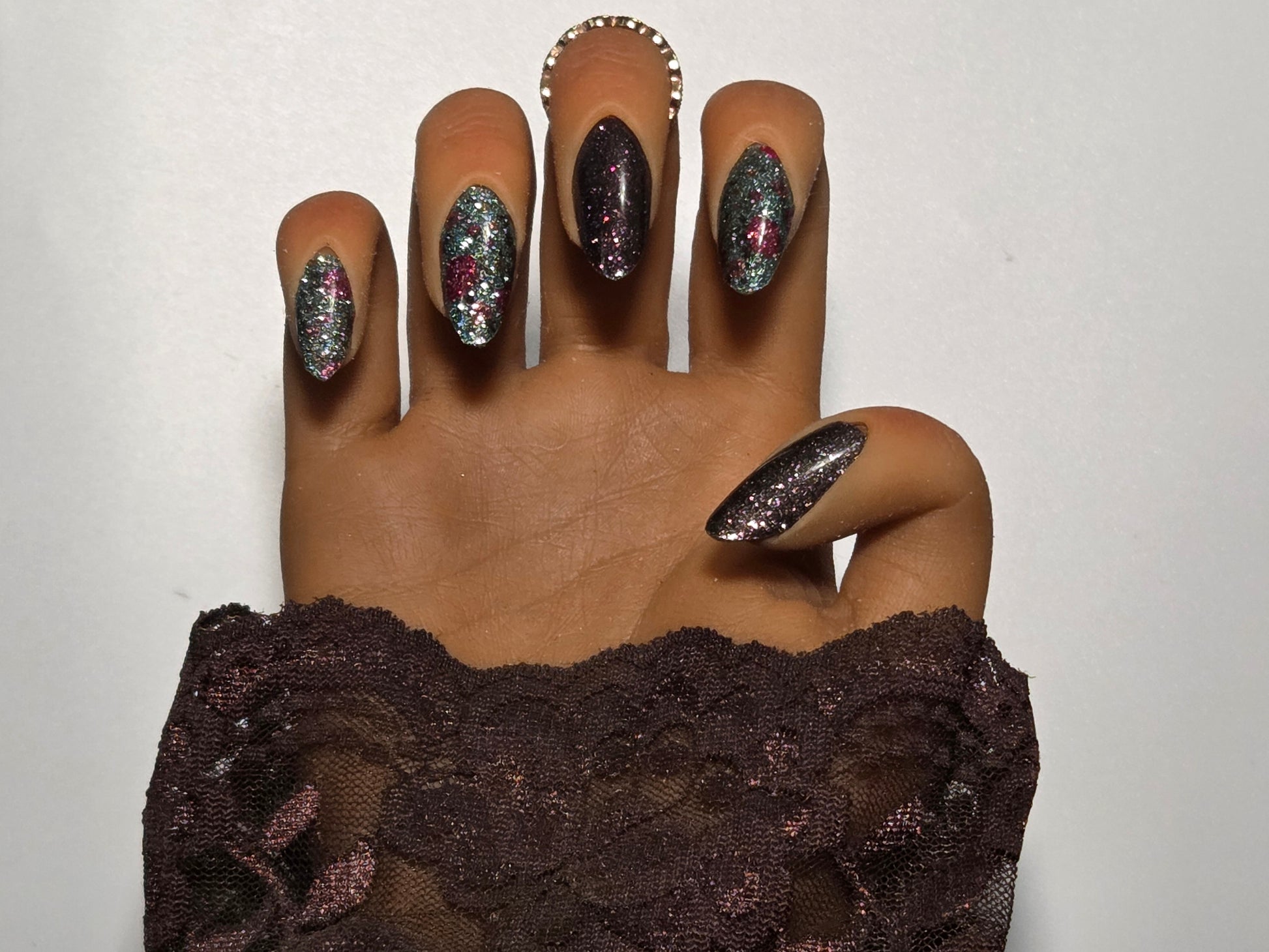 Hand with glittery nail wraps  wearing a brown lace garment against a white background