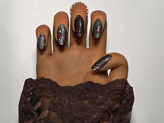 Hand with glittery nail wraps  wearing a brown lace garment against a white background