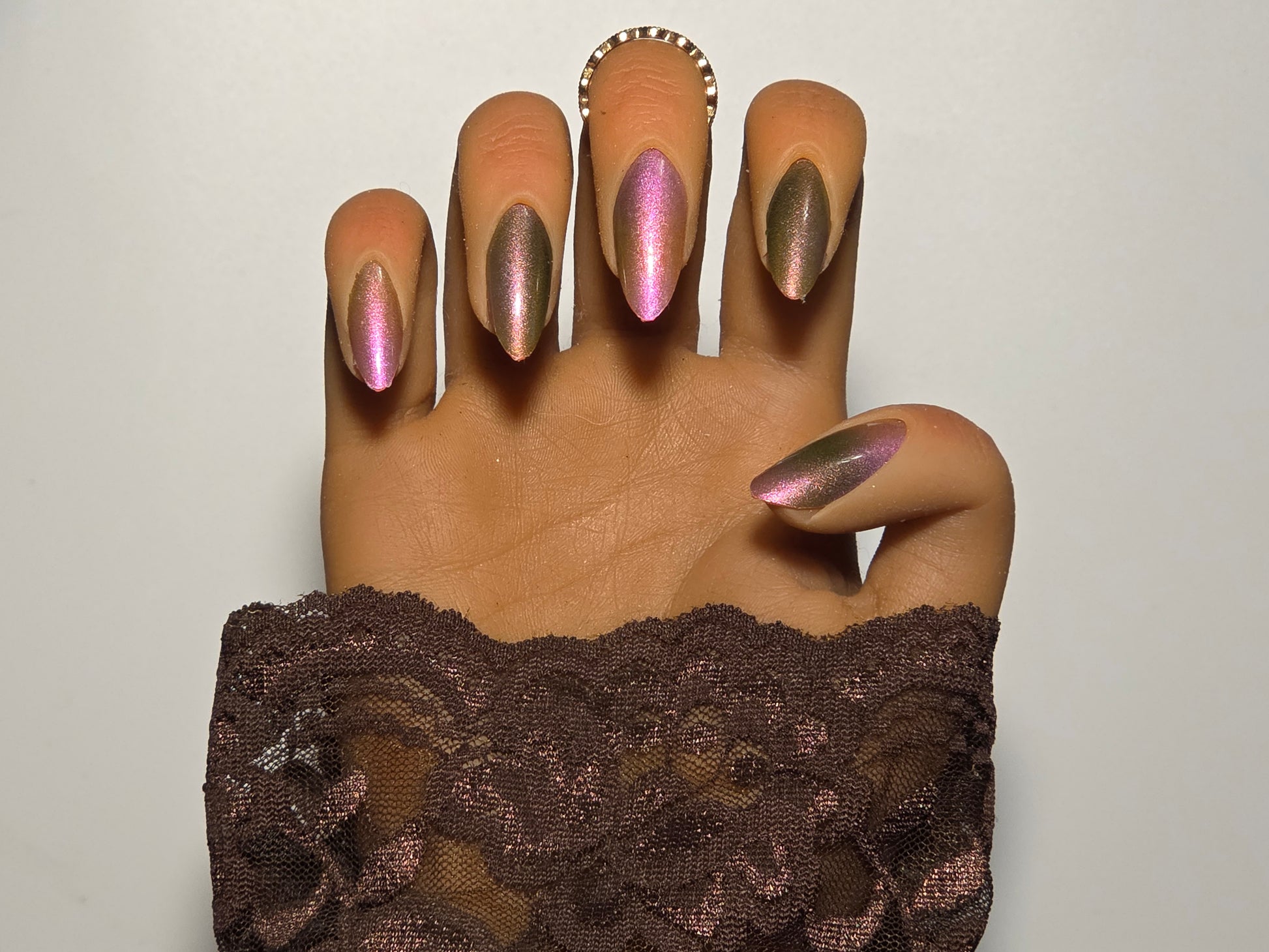 Hand with green and white aurora nail wraps over nail polish wearing a brown lace garment against a plain white background