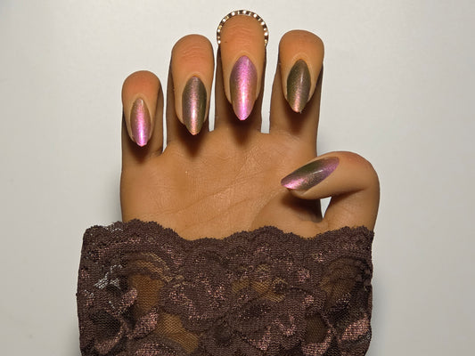 Hand with green and white aurora nail wraps over nail polish wearing a brown lace garment against a plain white background