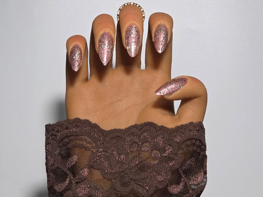 Hand with glittery Golden Handmade Press on Nails wearing a brown lace garment  background against a white background