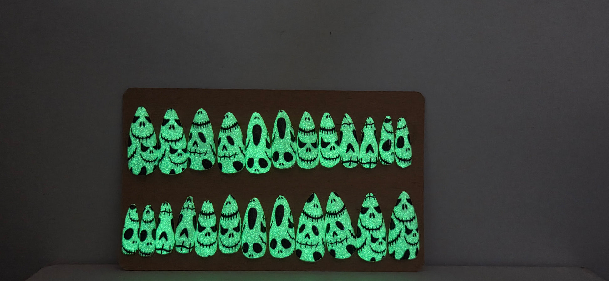 Glowing green skeleton  on a dark Press on Nails on a cardboard display against a plain background