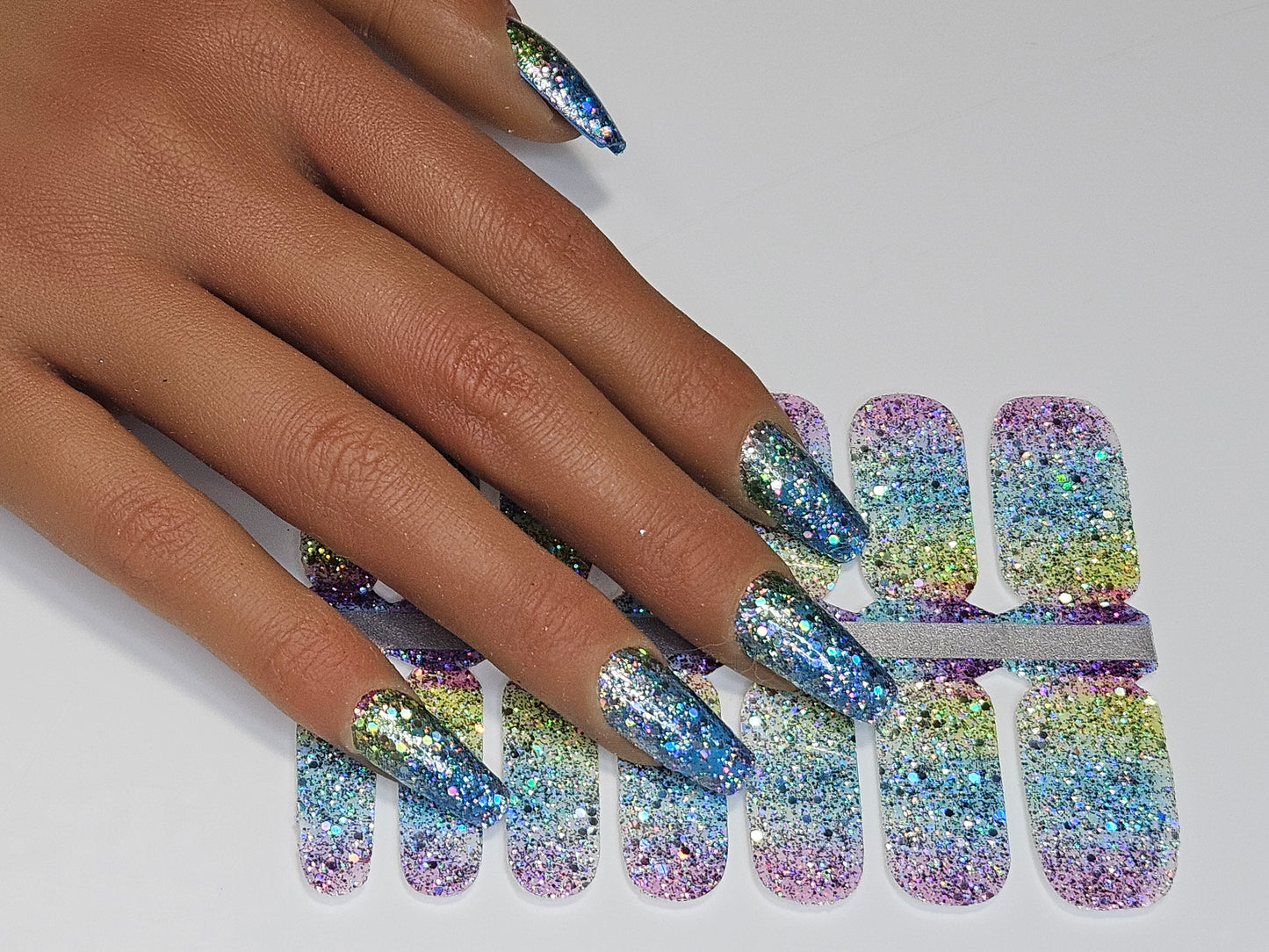 Multicolored glittery nail wraps on a hand with a white background