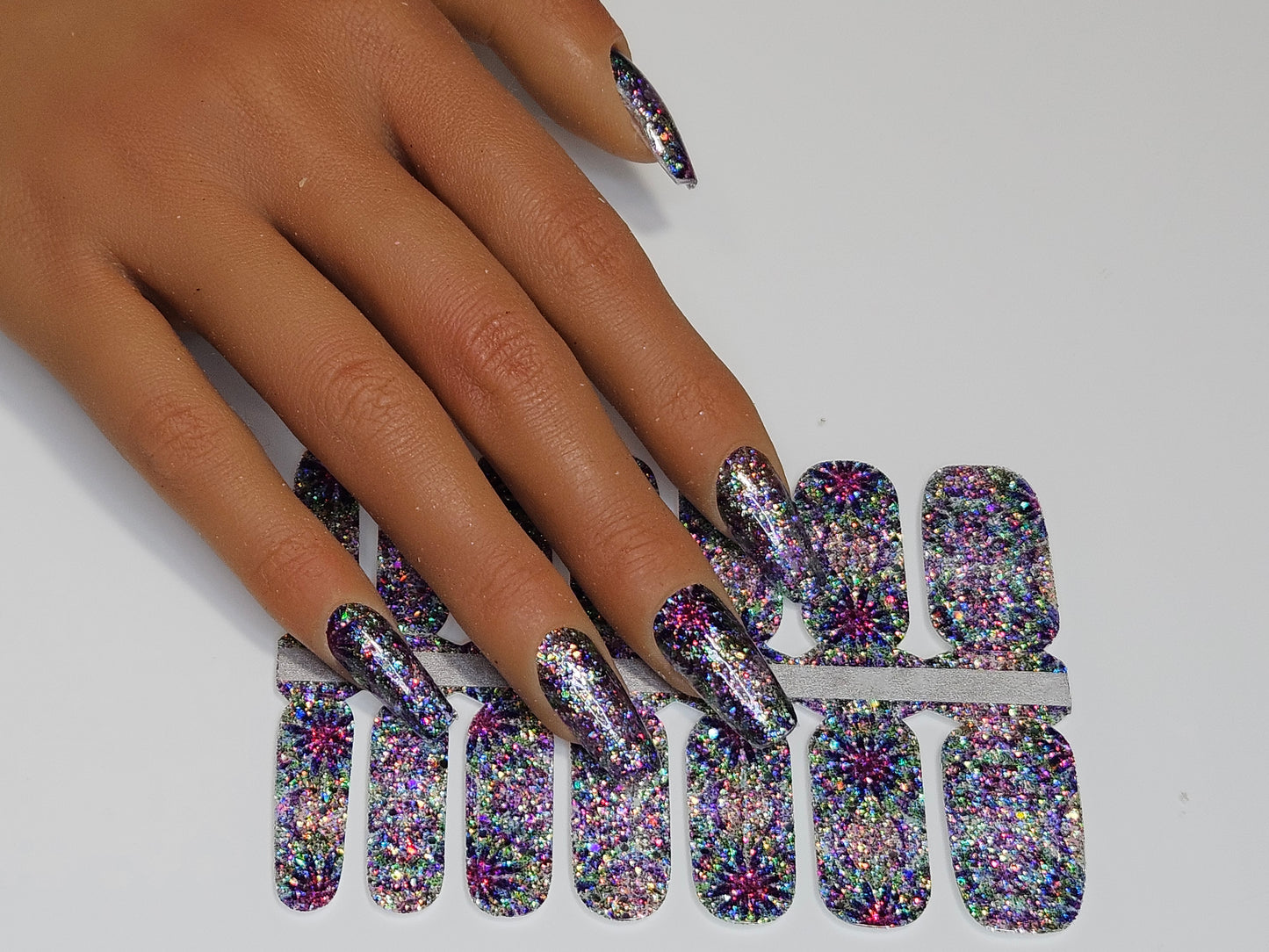 Multicolored glittery nail art sheets on a hand with a white background