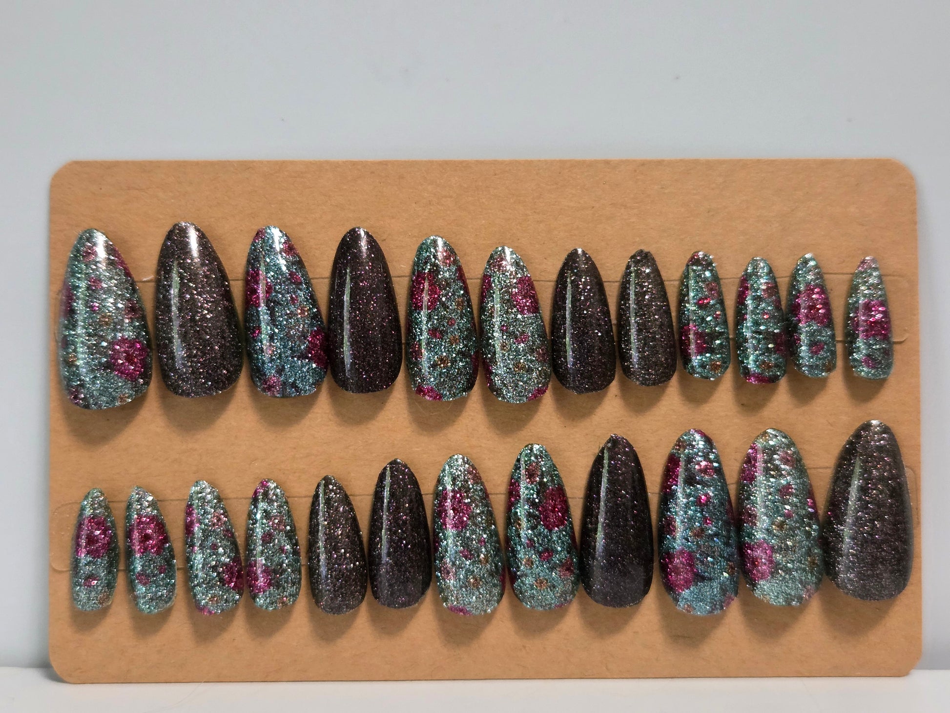 Set of glittery false nails on a piece of cardboard  with a plain background