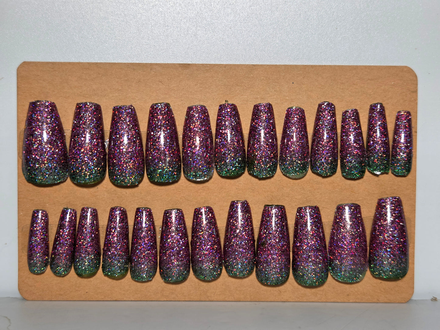 Set of purple and green glittery false nails on a cardboard display.