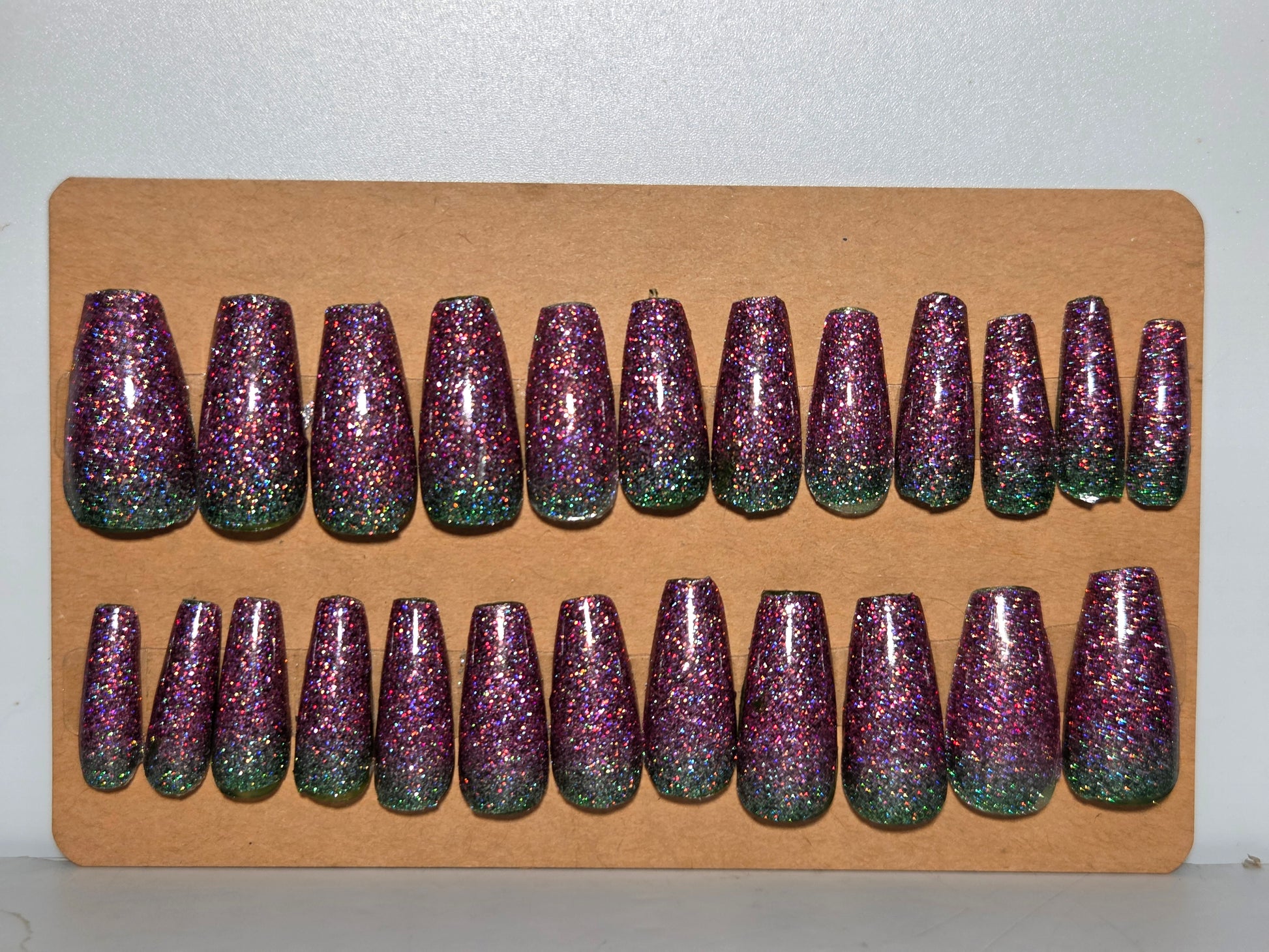 Set of purple and green glittery false nails on a cardboard display.