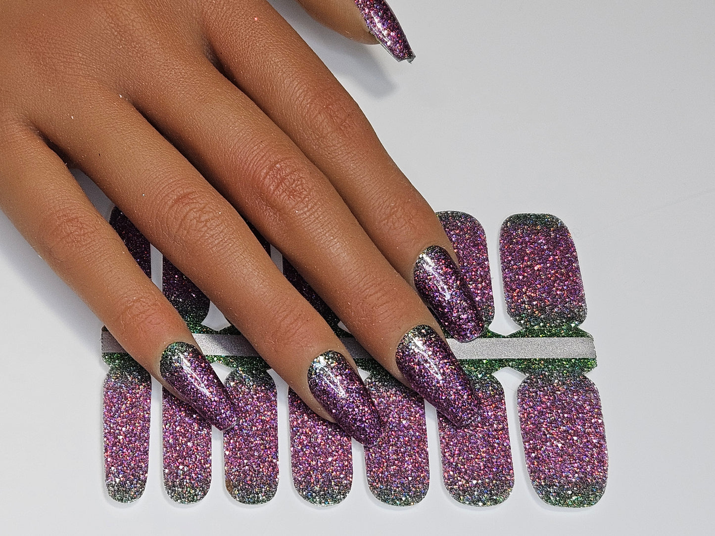 Hand with purple and green glittery nail wraps on against a white background