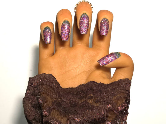 Hand with glittery pink nail wrap wearing a brown lace garment on a white background