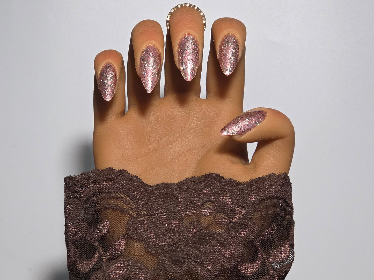 Hand with glittery Golden Handmade Press on Nails wearing a brown lace garment  background against a white background