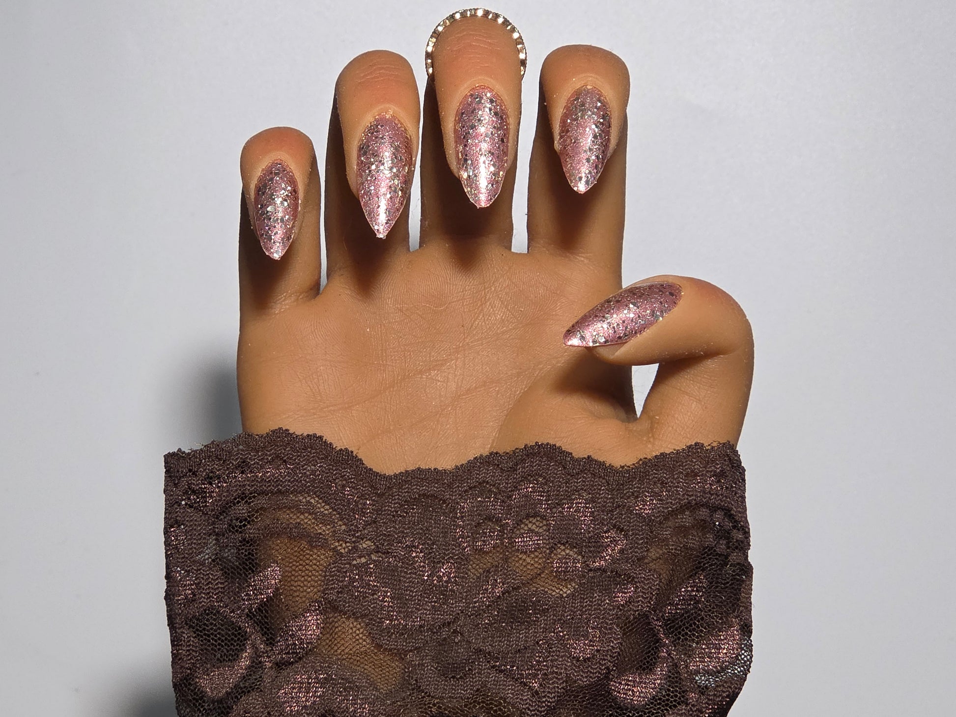 Hand with glittery Golden Handmade Press on Nails wearing a brown lace garment  background against a white background