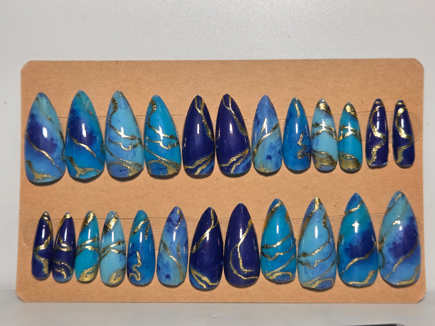 Set of multi colored blue with gold accents, handmade press on nails. On a cardboard display