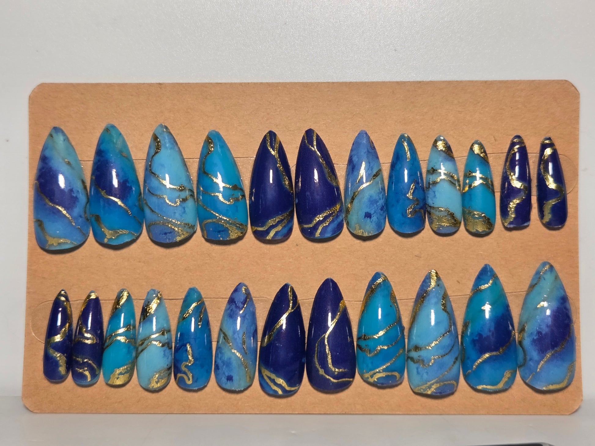 Set of multi colored blue with gold accents, handmade press on nails. On a cardboard display